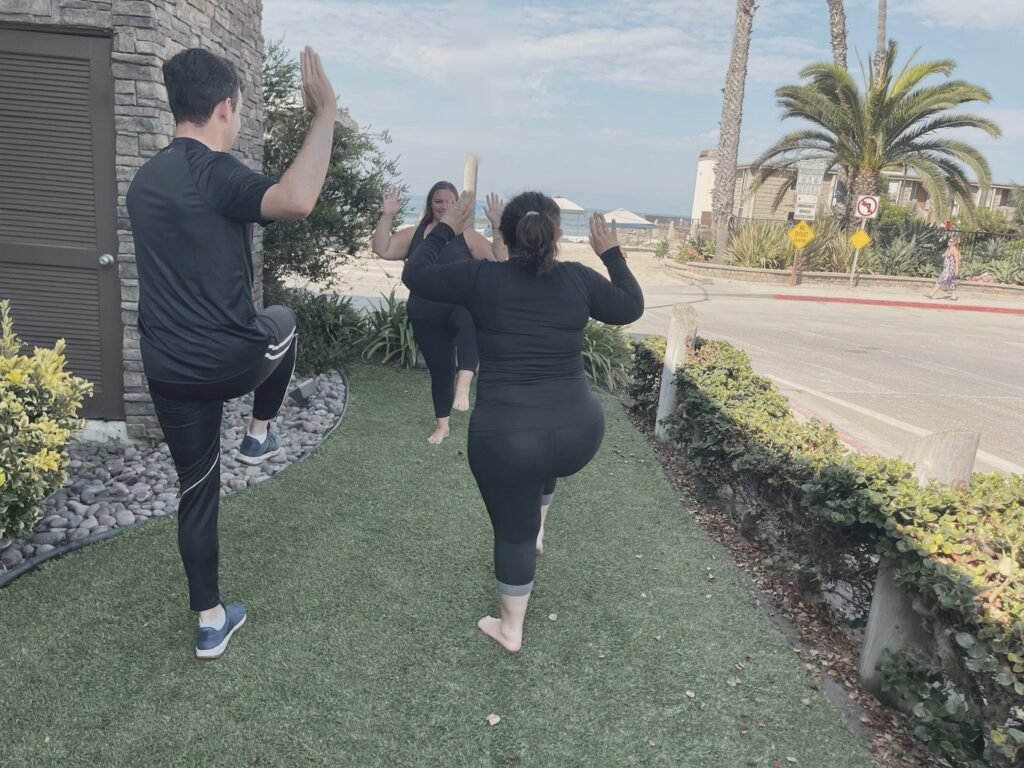 Three people balancing on one leg on a lawn beside the beach