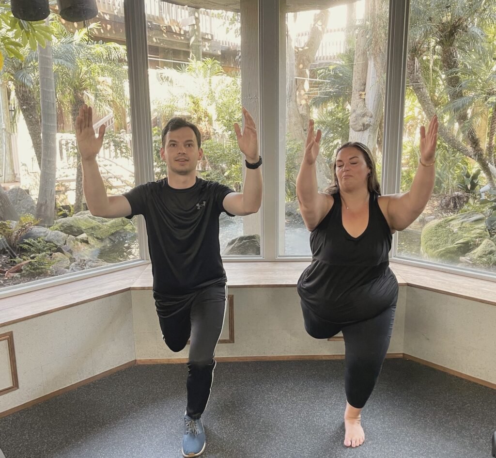 A man and a woman balancing on one leg with both arms raised