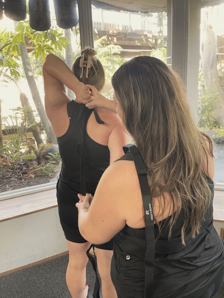 An instructor helping a woman with a strap stretch behind her back
