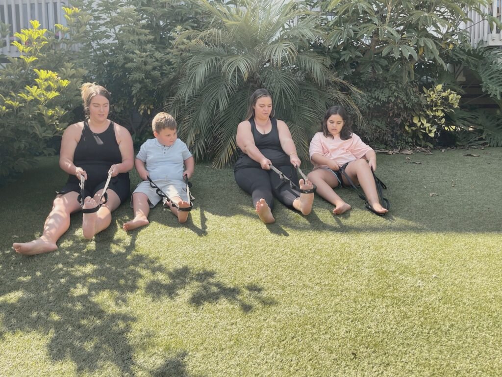 Two women and two children seated on the grass with stretch straps