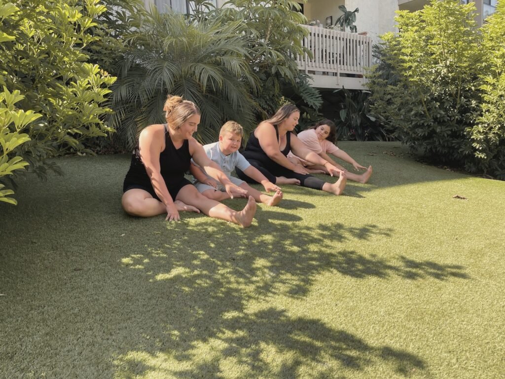 Two women and two children reaching for their toes on the grass, smiling