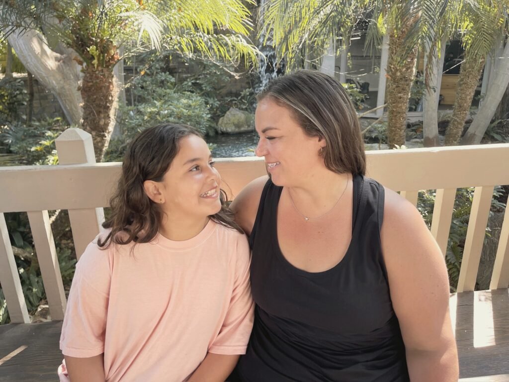 A woman and a girl smiling at each other on a garden bench