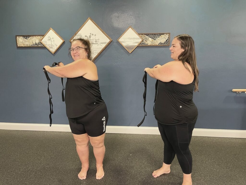 Two women holding stretch straps out in front of them in a studio